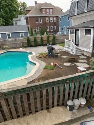 Backyard with pool, patio stones being laid, and a small shed beside a wooden fence