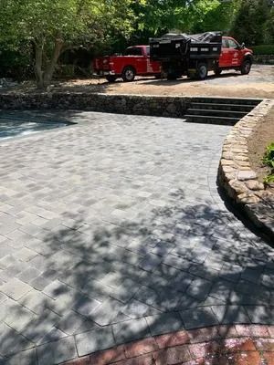 Stone-paved driveway with black and red trucks parked under trees beside a stone retaining wall