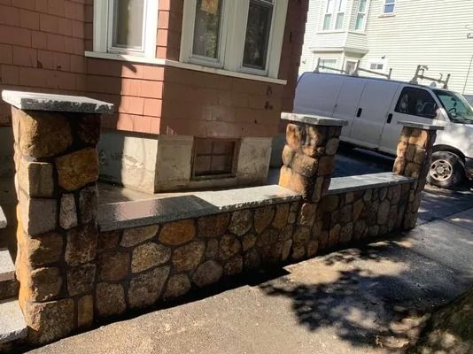Stone wall bench with square pillars along a sidewalk beside a building and parked van