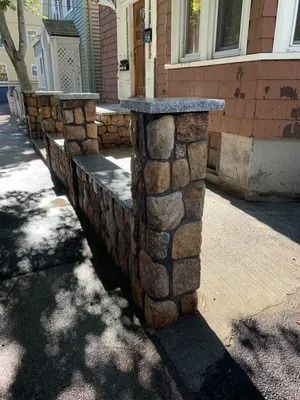 Stone front yard wall and railing beside a sidewalk next to a brick house