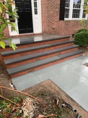 Front steps to a brick house with gray pavers and a white door.