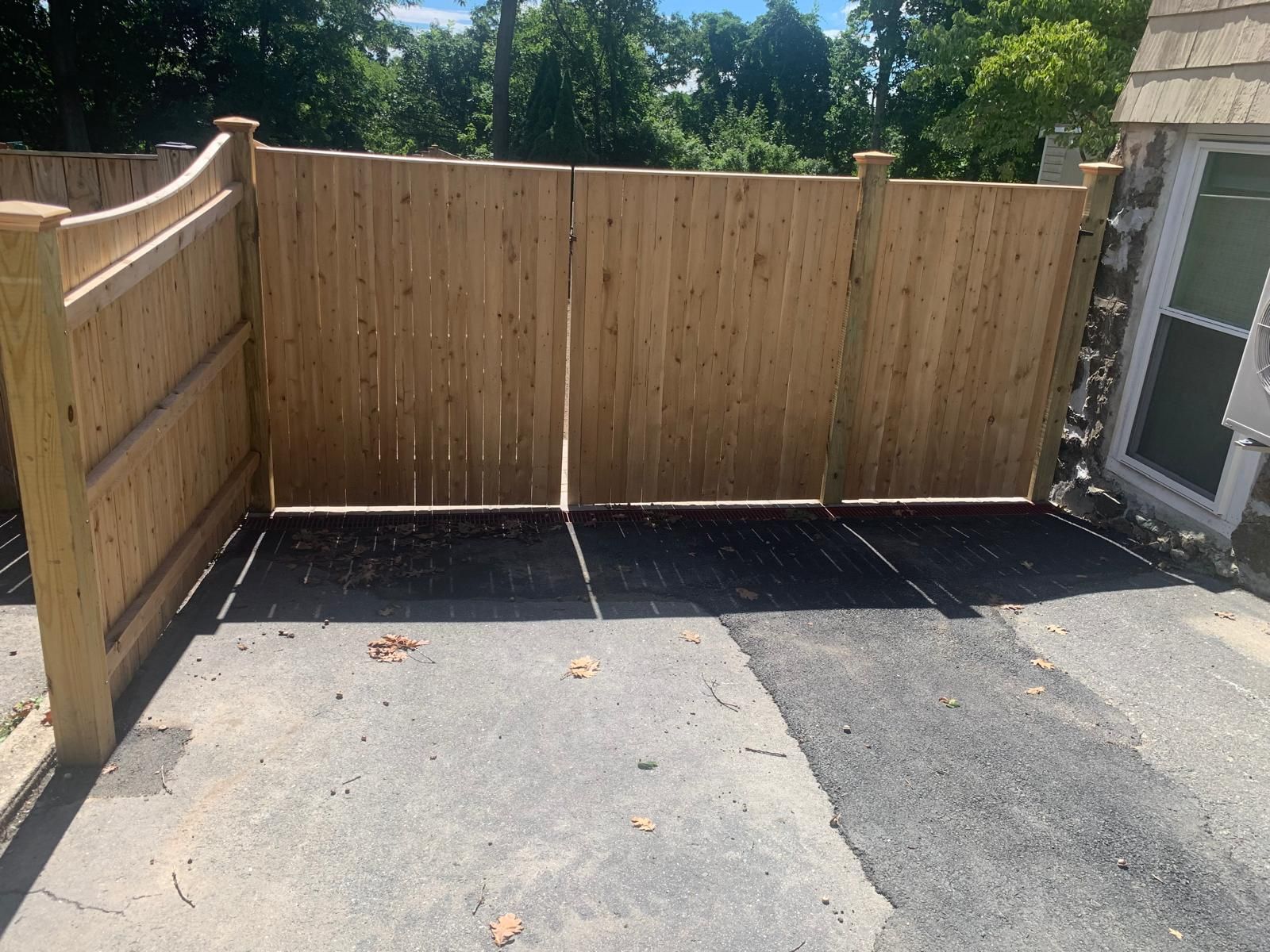 Wooden fenced corner with dark paving and light concrete driveway under bright sunlight
