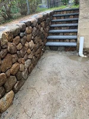 Stone retaining wall beside concrete steps and a sloped path outdoors