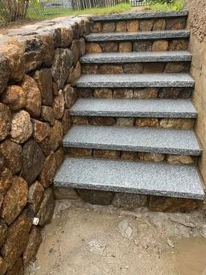 Stone steps beside a rough stone retaining wall leading up to a grassy path