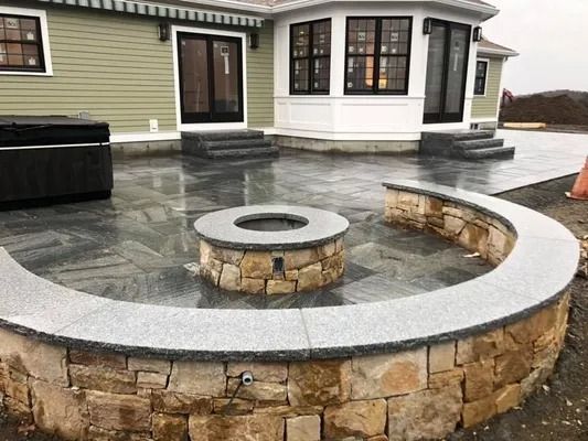 Stone circular fire pit and curved built-in bench on a wet patio outside a house