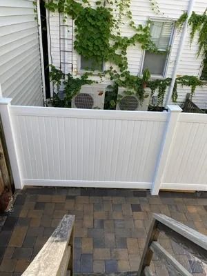 Backyard patio with paver stones, white vinyl fence, and green vines growing along the wall