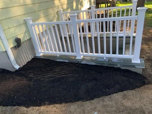 Fresh black mulch spread beside a white porch railing and steps by a house siding wall
