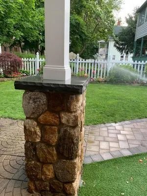 Stone porch column with white post on a green lawn beside a white picket fence and walkway