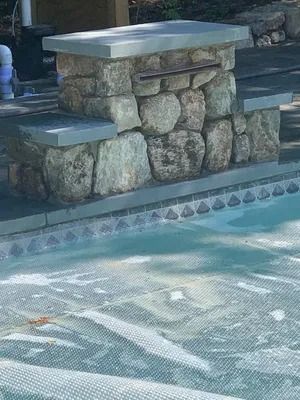 Stone poolside bench beside a blue swimming pool with patterned tile border