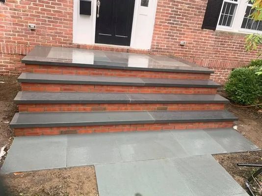Brick house entrance with wide concrete steps and red brick risers leading to a black door