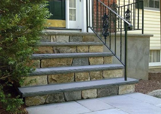 Stone steps leading to a front porch with black metal railing and a white door