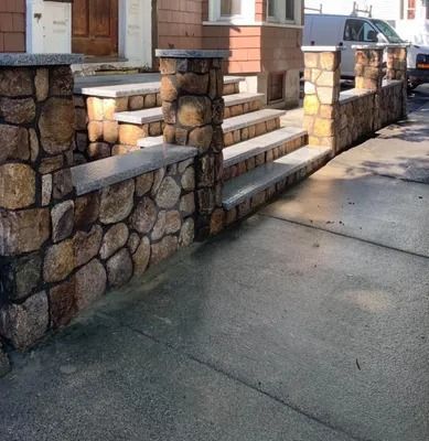Stone front steps and low wall beside a sidewalk in front of a house on a sunny street.