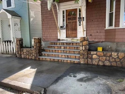Front porch with stone steps, brick facade, and white door beside a driveway.