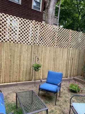Backyard patio with blue chairs, glass table, potted plants, and a wooden privacy fence with lattice top.