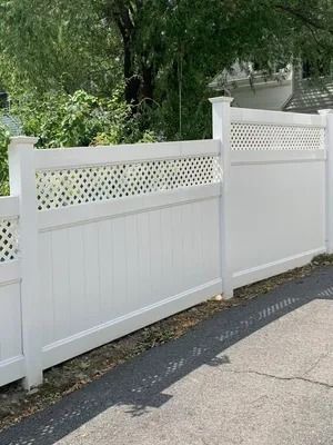 White picket fence with lattice panels along a roadside, with greenery behind it.