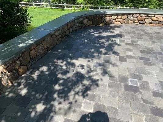 Stone patio with curved retaining wall and dappled tree shadows in a sunny yard