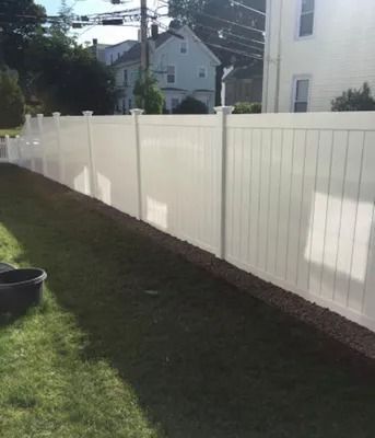 White vinyl fence along a narrow grassy yard beside a house, with neighboring homes in the background.