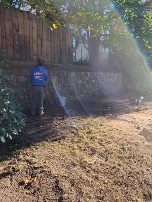 Person in blue shirt standing by a stone wall beside a sunlit dirt path with lens flare.
