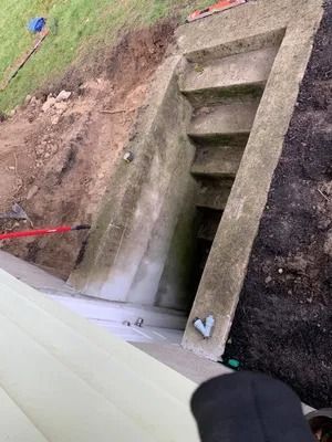 Concrete drainage culvert entrance in a dirt embankment with steps and a white barrier in the foreground