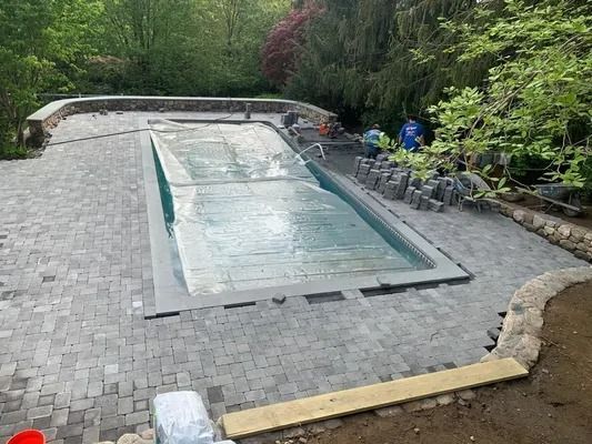 Outdoor stone patio with a rectangular water feature beside lush green trees and shrubs
