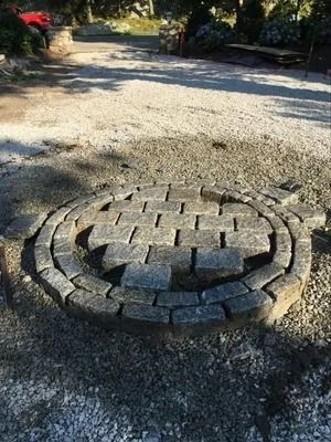 Circular stone planter in a gravel path, with a tree stump in the center and flowers in the background