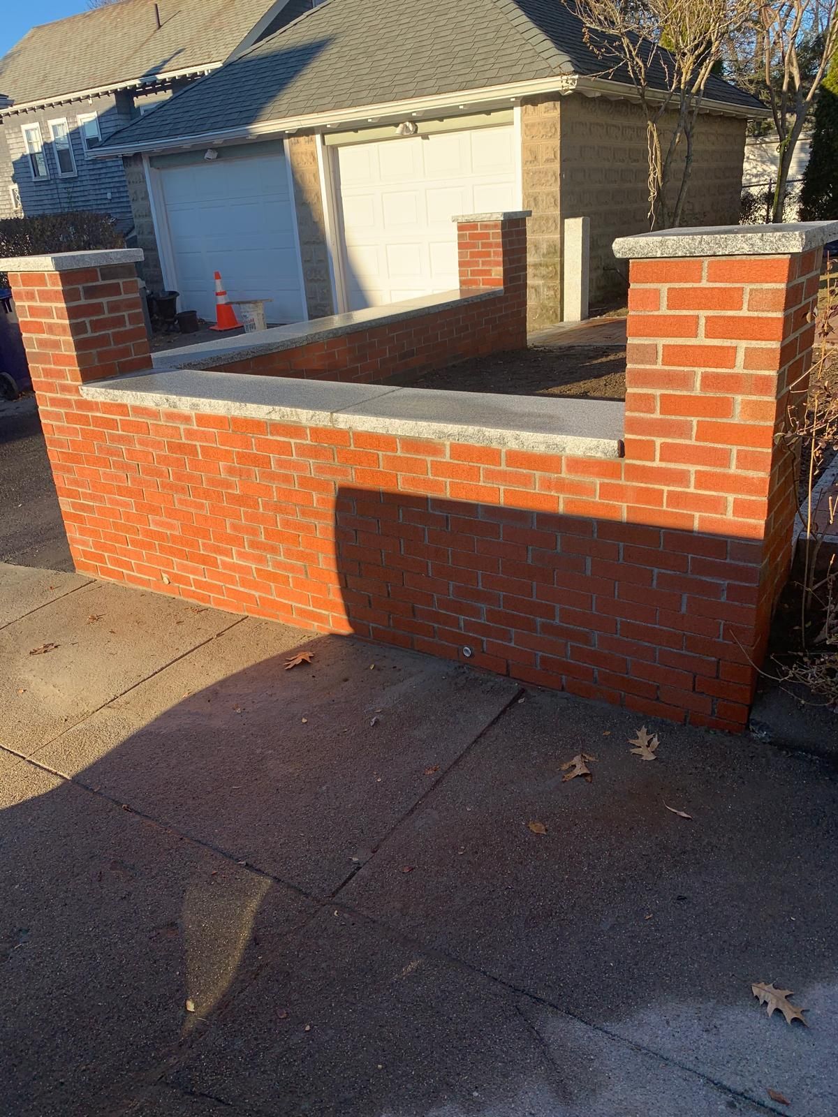 Brick wall and columns at a driveway entrance in front of a garage, with an orange traffic cone nearby.