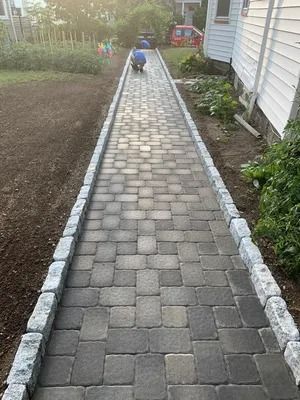 A paved garden walkway bordered by stone edging, with a person kneeling at the far end.