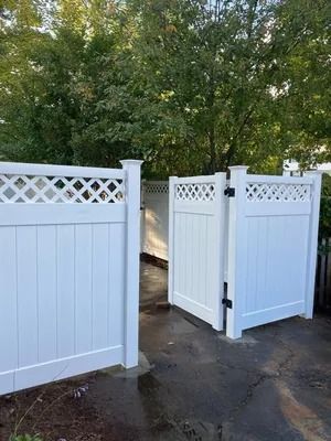 White lattice-top vinyl fence gate opening onto a paved path with trees behind it