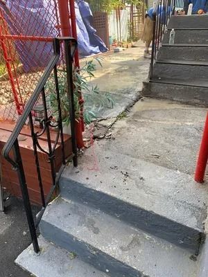 Concrete steps and a narrow ramp beside a red metal fence in an outdoor walkway.