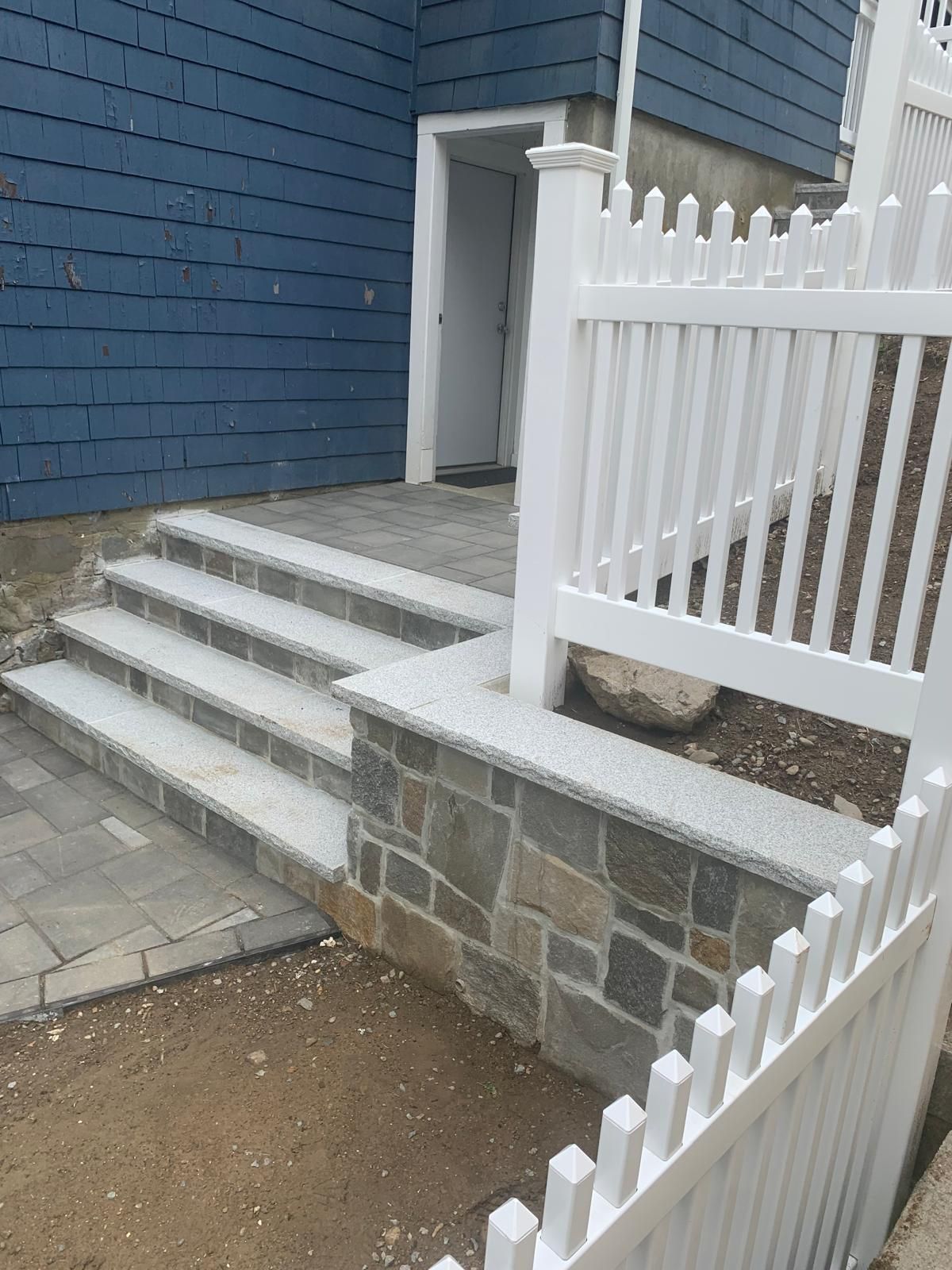 Front steps and white picket fence beside a blue house with stone retaining wall
