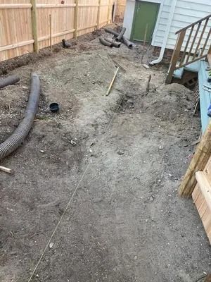 Backyard dirt lot with a fenced perimeter, exposed pipes, and a house deck on the right.