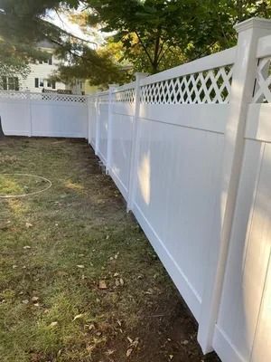 White vinyl privacy fence along a grassy yard with trees and a lattice top.