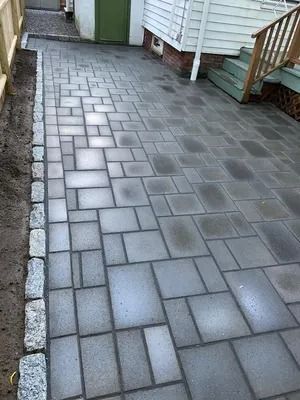 Gray brick paver walkway beside a white house and wooden steps