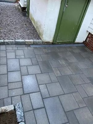 Gray brick patio beside a green door and white wall, with a gravel strip along the edge.