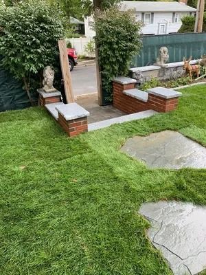 Garden gate with brick posts, a statue, and a green lawn leading to a patio area