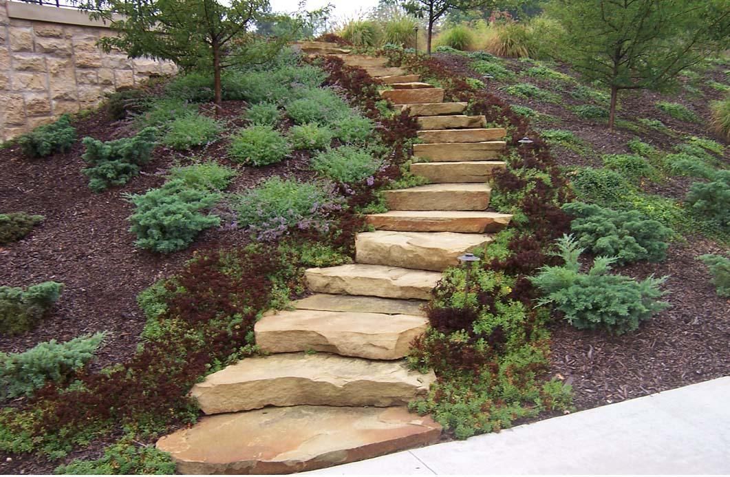 Stone garden steps leading up a landscaped hillside with green shrubs and mulch