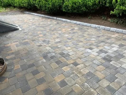 Stone-paved patio beside green bushes and a curb, with part of a planter visible at left.