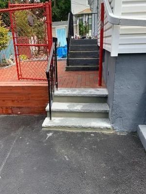 Front steps with concrete stairs leading to a red deck and chain-link fence beside a gray house.