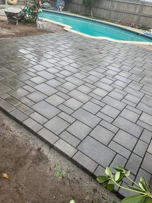 Gray stone patio beside a turquoise swimming pool, with a small plant in the foreground.