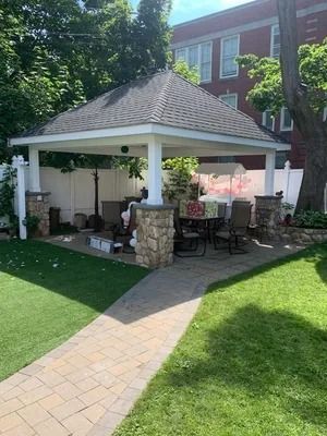 Backyard gazebo with stone columns, patio furniture, and a brick walkway beside a house