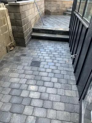 Narrow brick walkway with steps leading to a wet patio beside a black metal gate