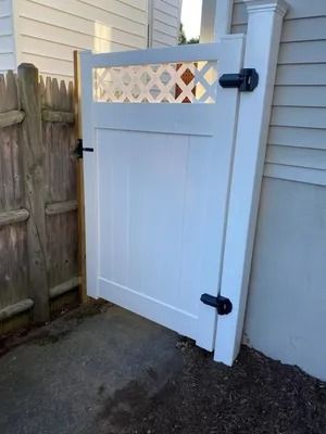 White backyard gate with black hinges beside a house and wooden fence.