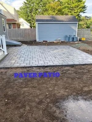 Backyard patio with gray paver area, dirt foreground, and blue shed by a wooden fence.