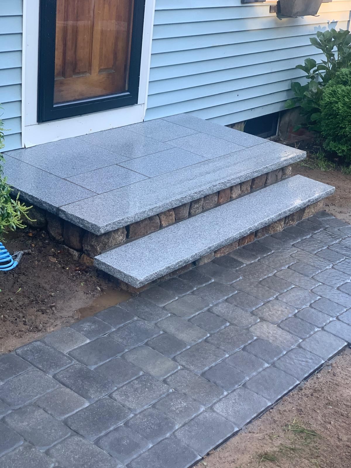 Front steps with a gray stone landing and single step beside a house with blue siding.