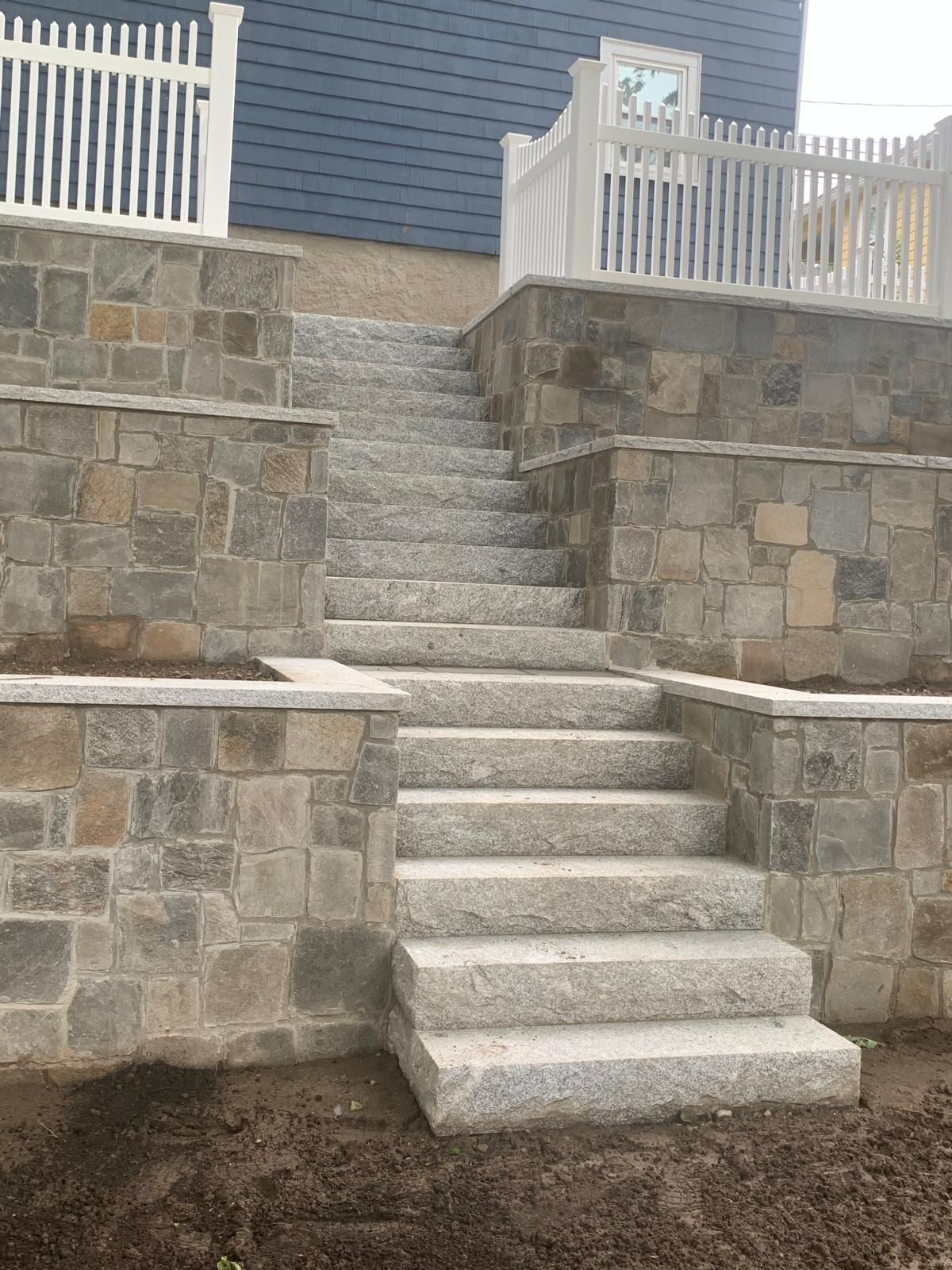 Stone steps built into a retaining wall leading up to a house deck with white railings