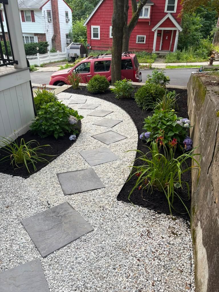 Curved stone walkway through a gravel garden leading to a red house and parked car on a residential street