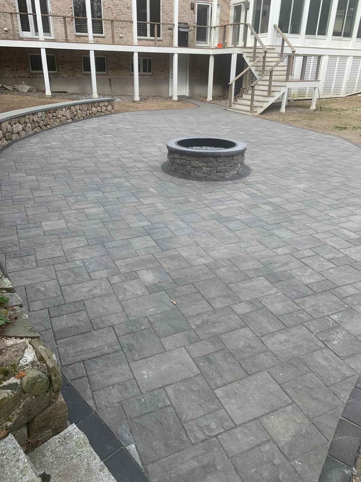 Circular stone patio with a central fire pit in a courtyard beside a house