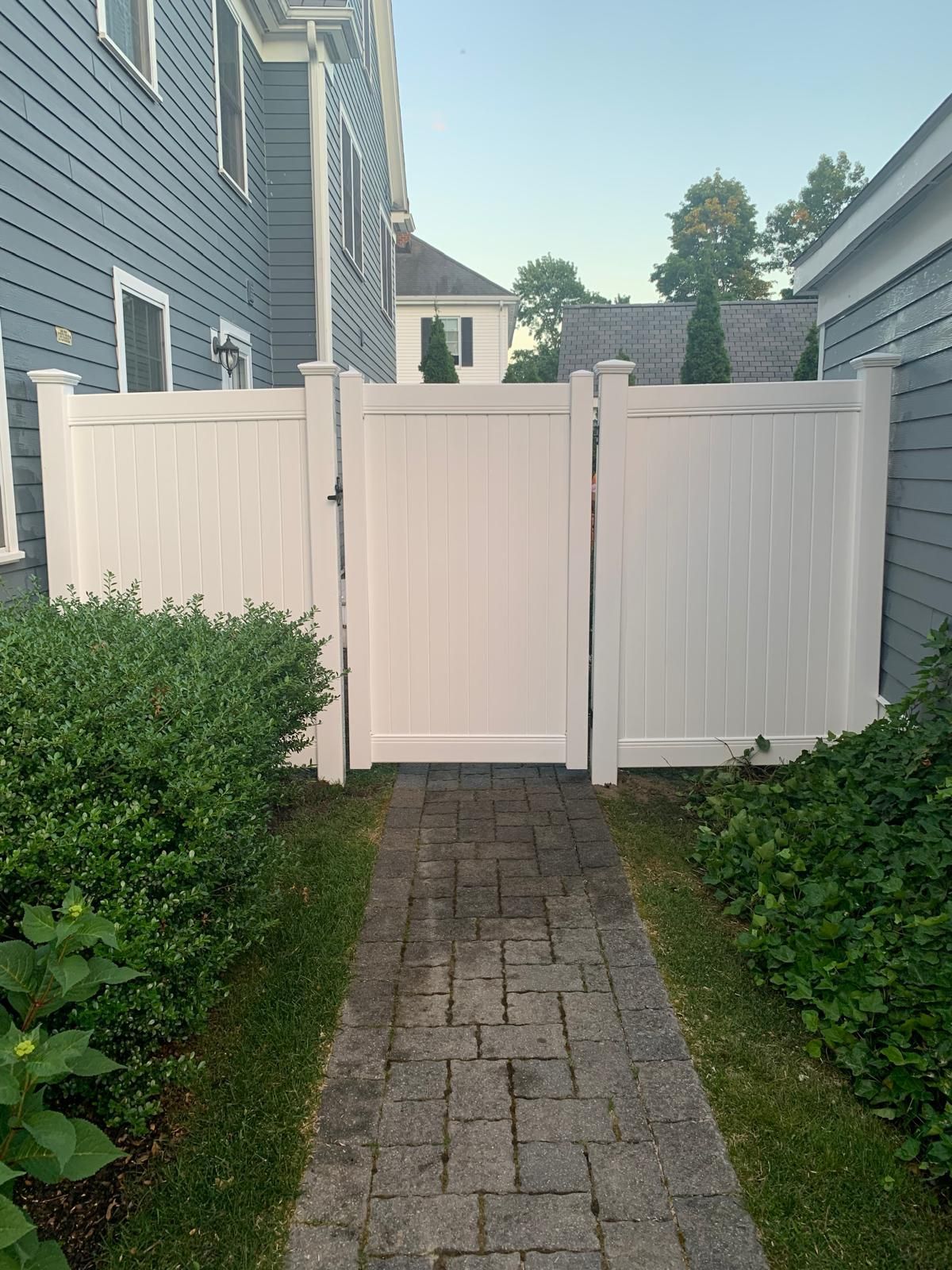White vinyl privacy gate along a brick walkway between two houses in a narrow side yard