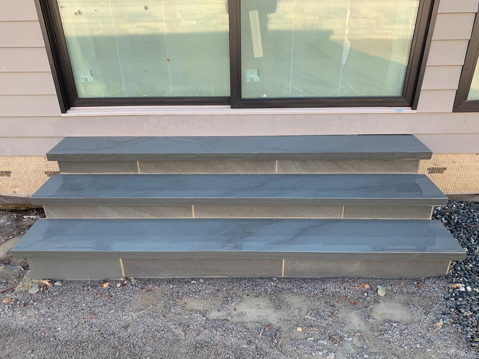 Three gray steps leading to a sliding glass door beside a gravel path.