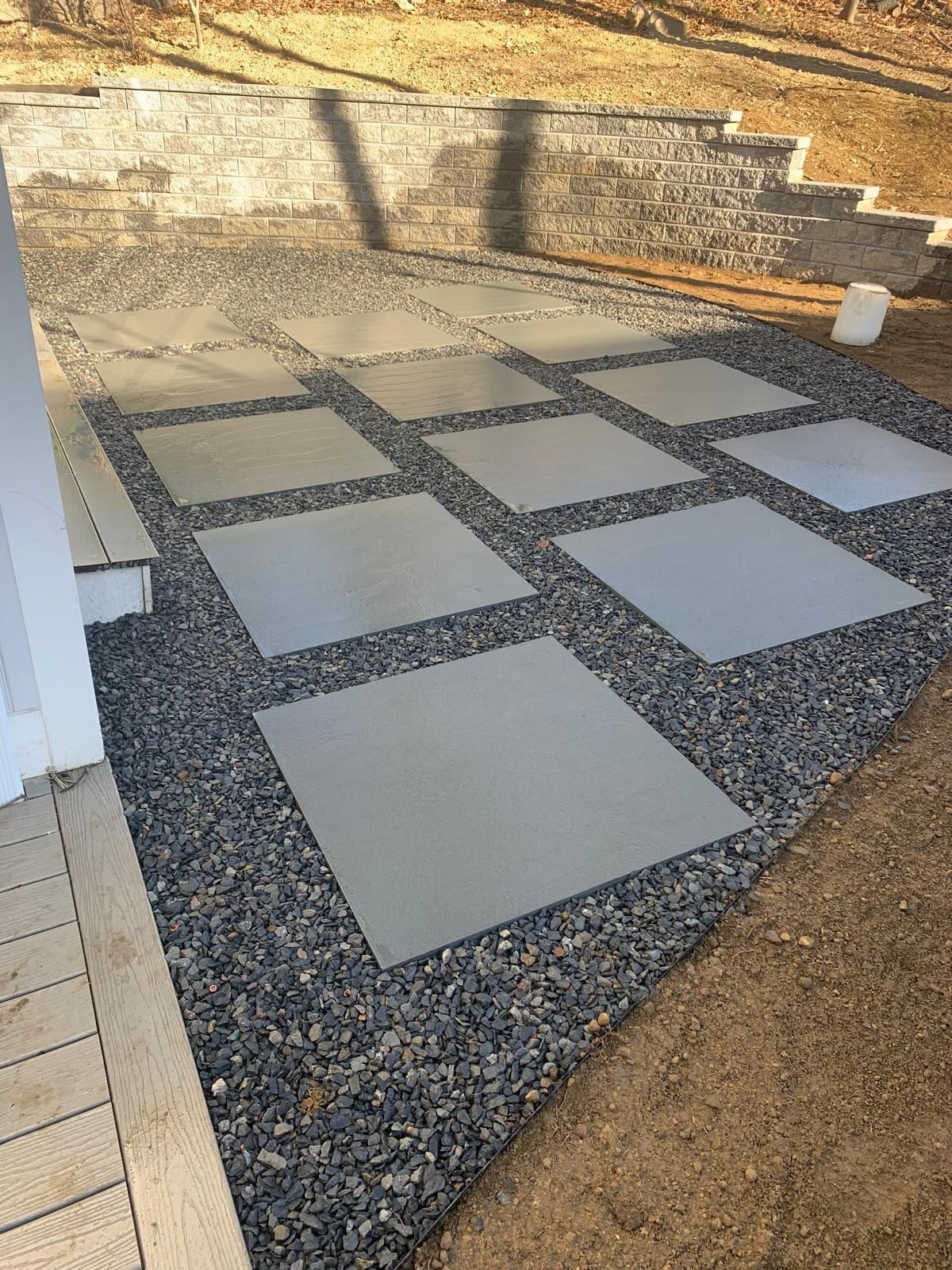 Patterned stone patio with large square pavers set in dark gravel beside a brick wall and steps.
